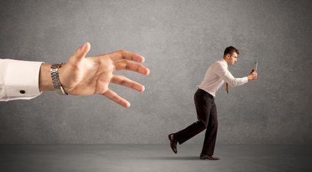 Young miniature businessman running from a big hand with light grey background