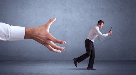 Young miniature businessman running from a big hand with blueish grey background