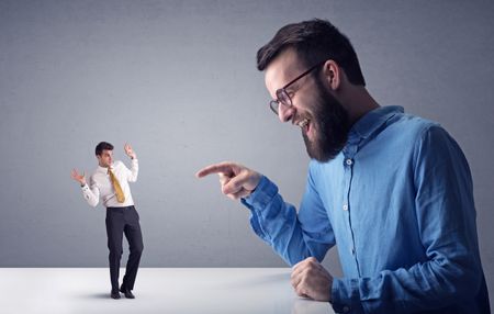 Young professional businessman being angry with an other miniature businessman in front of a grey background