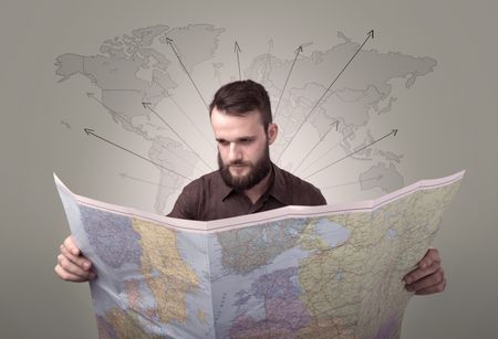 Handsome young man holding a map with world map and arrows behind him