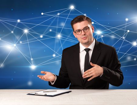 Young handsome businessman sitting at a desk with a blue connection graphic behnid him