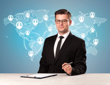Young handsome businessman sitting at a desk with a blue world map behind him
