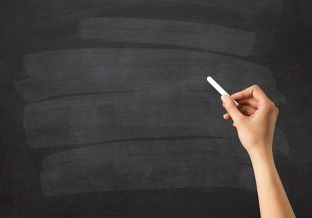 Female hand holding white chalk in front of a blank blackboard