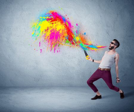 A funny hipster person in casual urban clothing shouting bright colorful paint on city wall concept