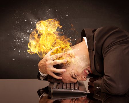 A depressed businessman banging his head in a keyboard and shouting with his head on fire, reflecting on desk