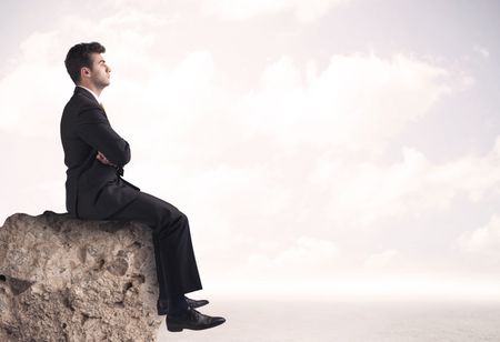 A young sales person in elegant suit sitting with paper on top of a stone in the clouds concept