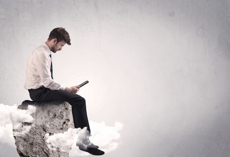 An elegant  smart businessman with laptop sitting in empty grey space on top of a cliff, between clouds concept
