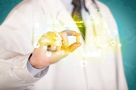 A doctor in white coat with a stethoscope on one shoulder holding a pill with green glowing graphs, lines, numbers, charts, between his fingers