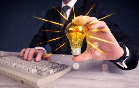 A male business person holding an electric light bulb in his hand with beam rays illustration concept.