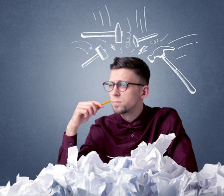 Young businessman sitting behind crumpled paper with drawn hammers hitting his head