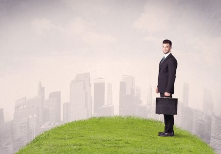 A confident male well looking office manager standing in small green grass in front of city landscape with tall buildings concept.