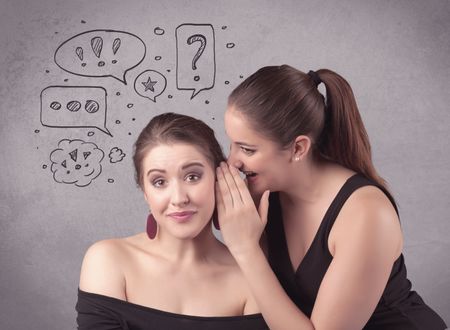 Two girls chatting and sharing their secrets concept with drawn chat bubbles on the background urban wall.