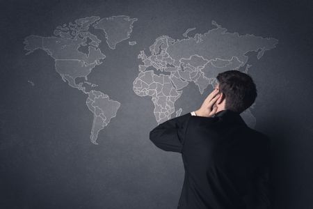 Young businessman in black suit standing in front of a black world map 