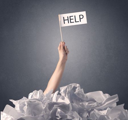 Female hand emerging from crumpled paper pile holding help sign 