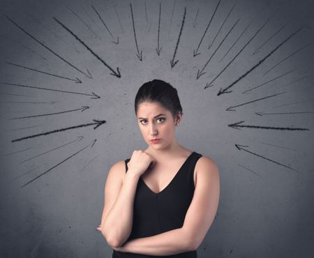 A teenage student girl under pressure while making happy face expressions illustrated with black arrows pointing at her head on the wall blackground concept.