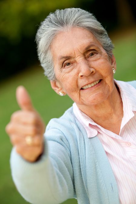 Lovely old woman with thumbs up and smiling outdoors