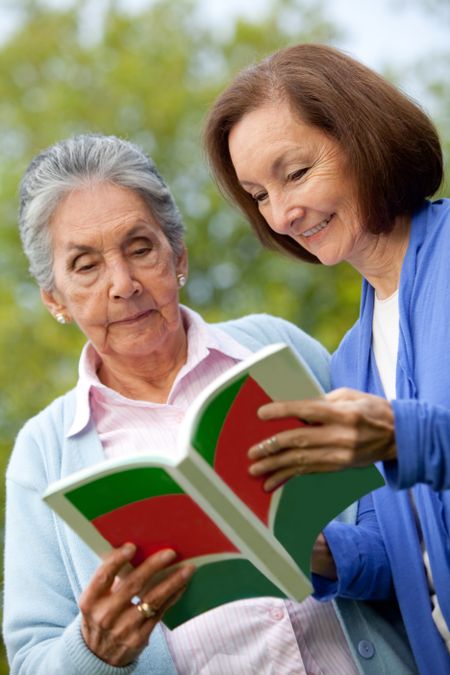 Portrait of an elder mother and daughter reading a book outdoors