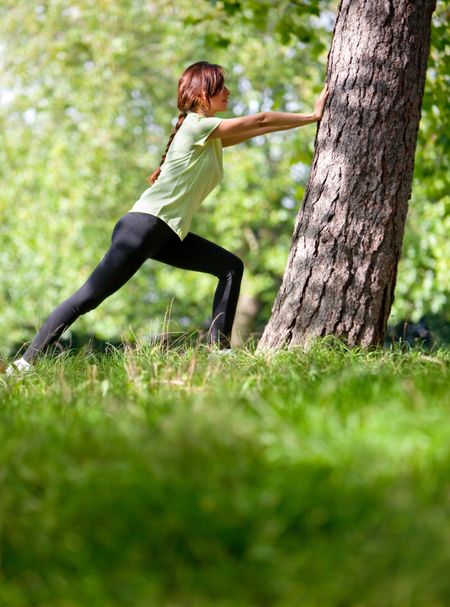 Woman stretching at the park next to a tree - fitness concepts