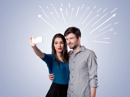 A cheerful young couple taking selfie photo with mobile phone and white lines and arrows pointing to the sky above them concept