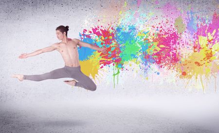 Modern street dancer jumping with colorful paint splashes on back wall concept