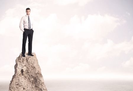 Successful sales person with brief case standing on top of a mountain cliff edge looking above the landscape between the clouds