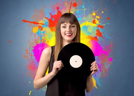 Young lady holding vinyl record on a grey background with colorful splashes behind her