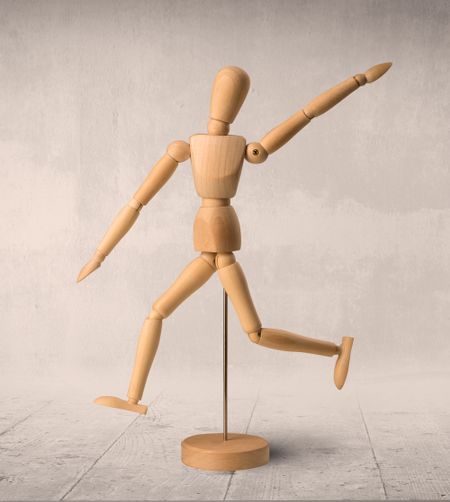 Wooden mannequin posed in front of a greyish background