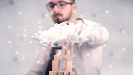 Young handsome businessman using wooden building blocks behind cloud concept 