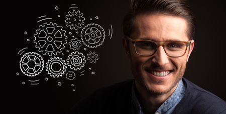 Portrait of a young businessman with rotating gears next to him on a dark background