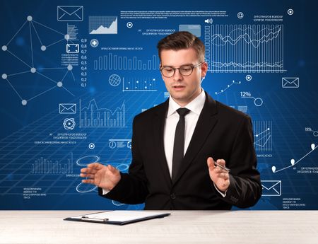 Young handsome businessman sitting at a desk with blue charts and data behind him