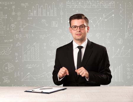 Young handsome businessman sitting at a desk with white graphs and calculations behind him 