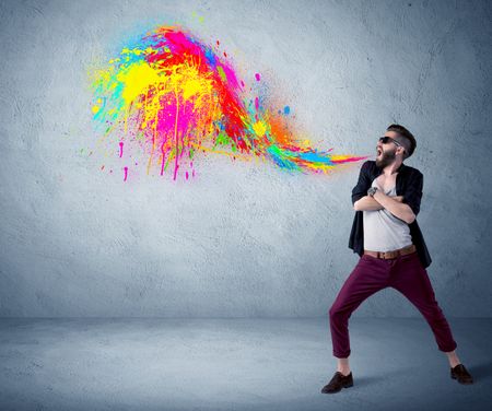 A funny hipster person in casual urban clothing shouting bright colorful paint on city wall concept