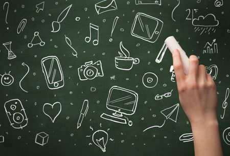 A person drawing media and communication icons on school blackboard with chalk