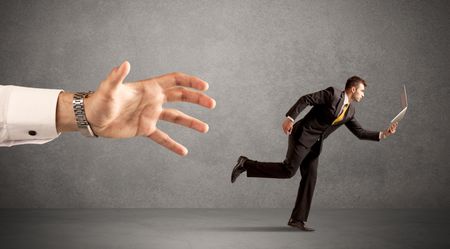 Young miniature businessman running from a big hand with light grey background