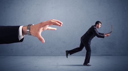 Young miniature businessman running from a big hand with blueish background