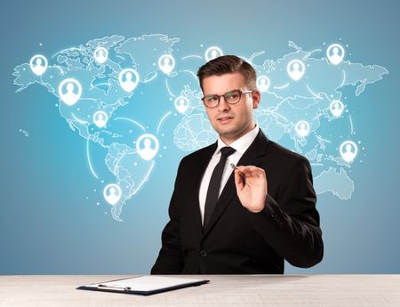 Young handsome businessman sitting at a desk with a blue world map behind him