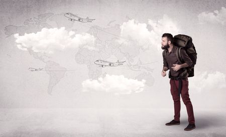 Handsome young man standing with a backpack on his back and planes in front of a world map as a background 