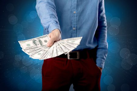 Young businessman holding large amount of bills with shiny blue background
