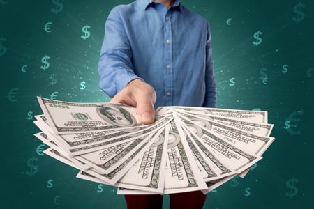 Young businessman holding large amount of bills with green background and currency symbols