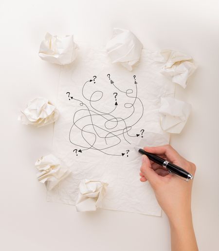 Female hand next to a few crumpled paper balls drawing random scribbles 
