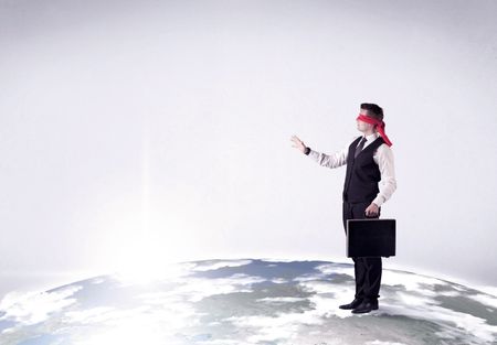 Young blindfolded businessman steps on a realistic globe