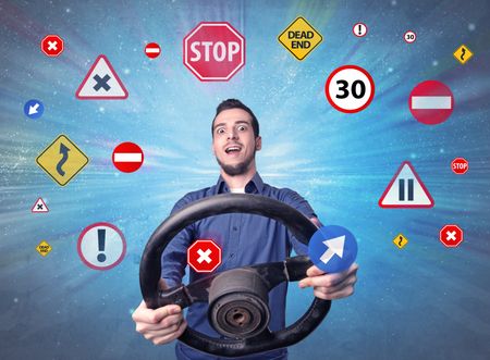 young-man-holding-black-steering-wheel-628100351 Young man holding black steering wheel with road signs surrounding him