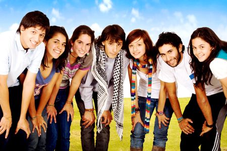group of happy friends smiling for a portrait in a park with green grass and a blue sky in the background