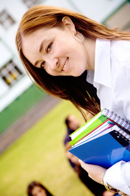 female teacher at a university carrying notebooks and smiling