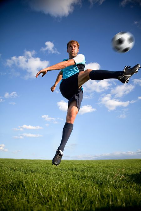 Male football player kicking the ball in the air