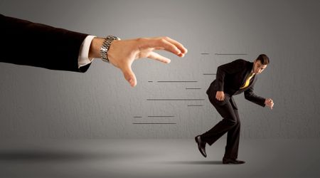 Businessman running away from a huge hand concept on background