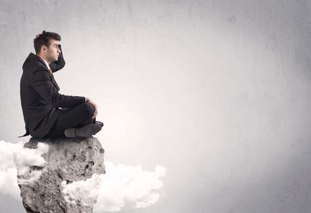 An elegant  smart businessman with laptop sitting in empty grey space on top of a cliff, between clouds concept