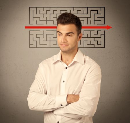 A young handsome business person making facial expression and solving maze with red arrow in front of clear, empty concrete wall background concept