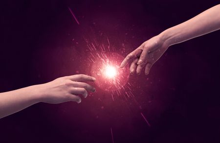 White caucasian male hands reaching out with fingers almost touching in bright red light sparkle in empty space background concept