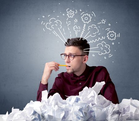 Young businessman sitting behind crumpled paper with drawings of gears and steam over his head